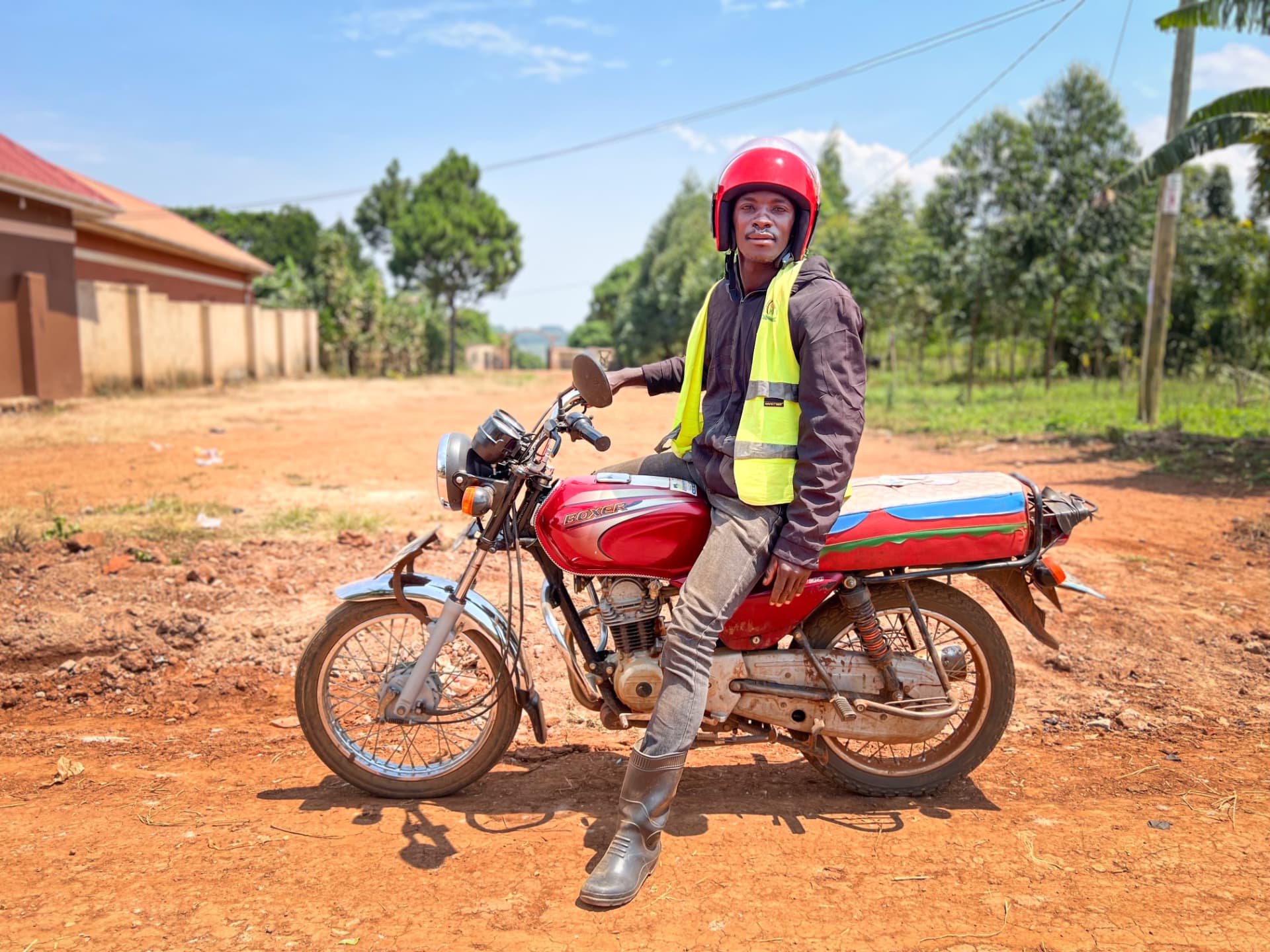 A boda-boda rider wearing a helmet and reflective vest beside his motorcycle